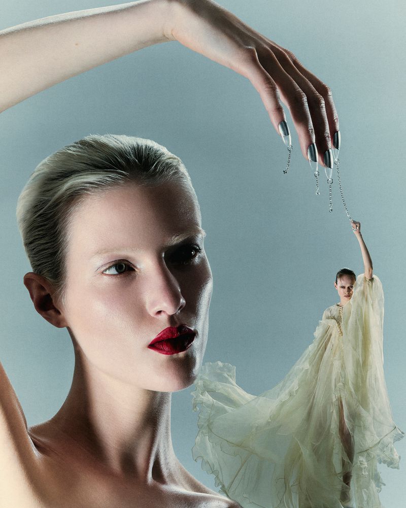 Conceptual beauty shot featuring a model with red lipstick and a large hand holding a chain above a smaller model in a flowing white gown.