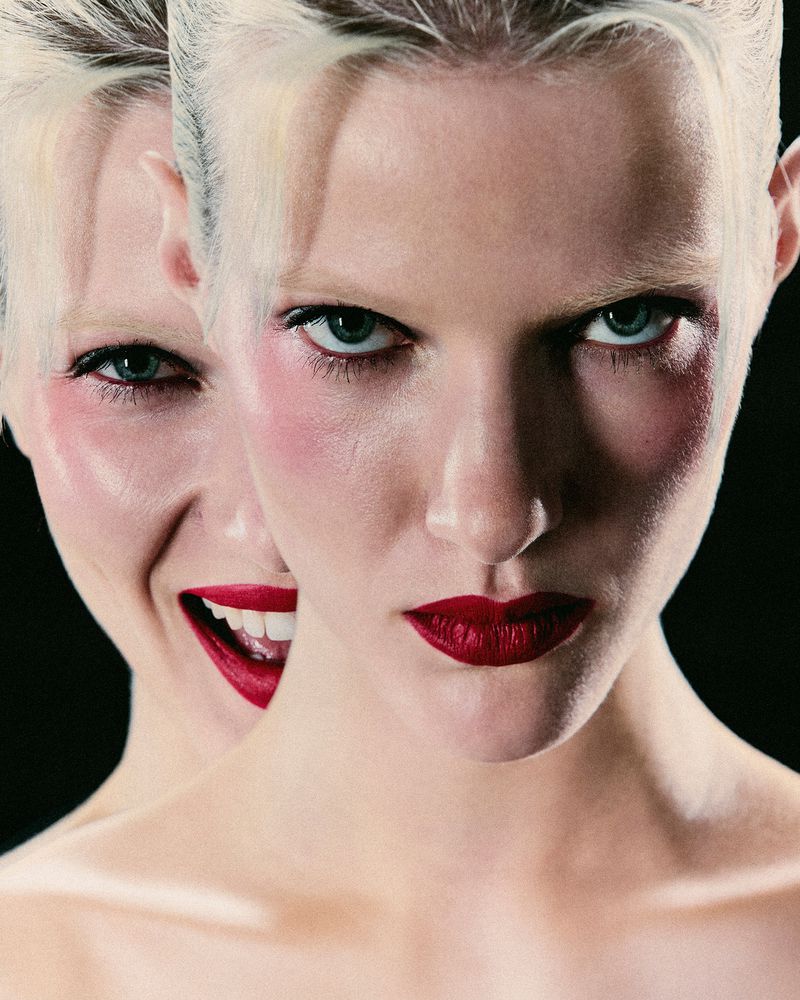 Conceptual beauty shot featuring a fair-skinned adult woman with short blonde hair and red lipstick against a stark black background.