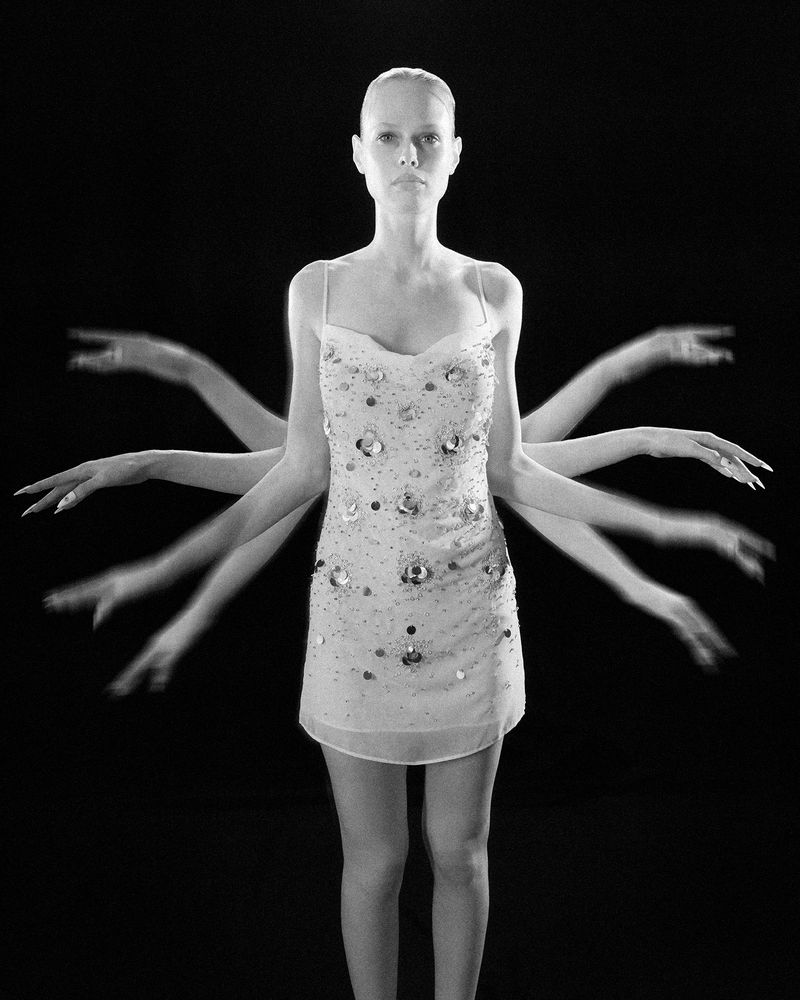 Black-and-white studio shot of a woman in a dress with a blurred motion effect creating the illusion of multiple arms.