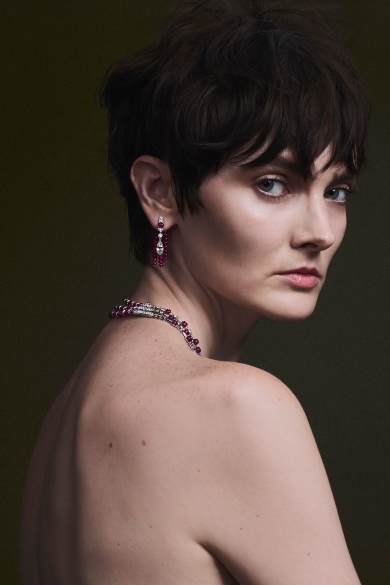 Model with short dark hair wearing ruby earrings and a beaded necklace against a dark background for L'Officiel Chile