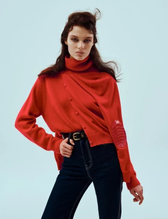 Model wearing a red turtleneck sweater and dark trousers against a light blue studio background for 10 Magazine USA.