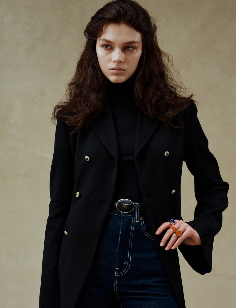 Model in black blazer and dark jeans wearing rings against a textured background for 10 Magazine USA