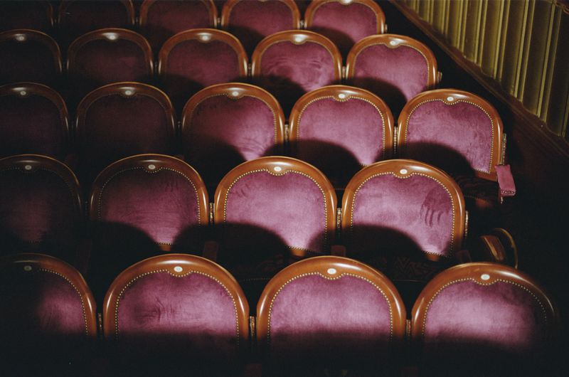 Rows of velvet auditorium seats in deep purple with wooden trim inside a theatre venue