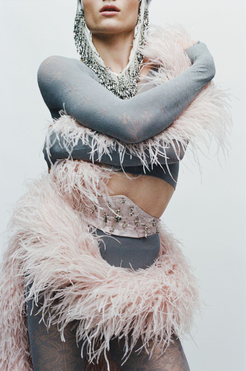 Model wearing a grey patterned top with pink feather boa and silver beaded headpiece against a plain white background