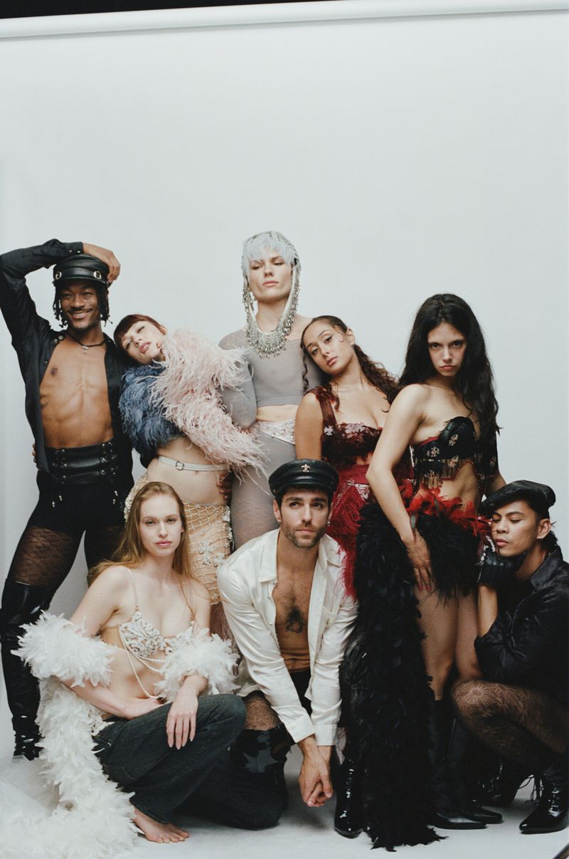 Group of diverse models posing together in eclectic fashion attire against a white studio background.