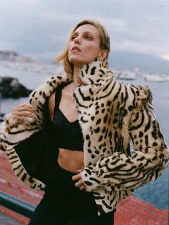 Model Anja Rubik wearing a leopard print jacket and black crop top outdoors by the water for Financial Times HTSI Magazine