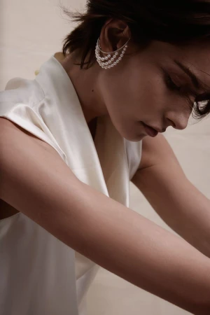 Model wearing a multi-strand pearl ear cuff and a white silk top against a neutral backdrop