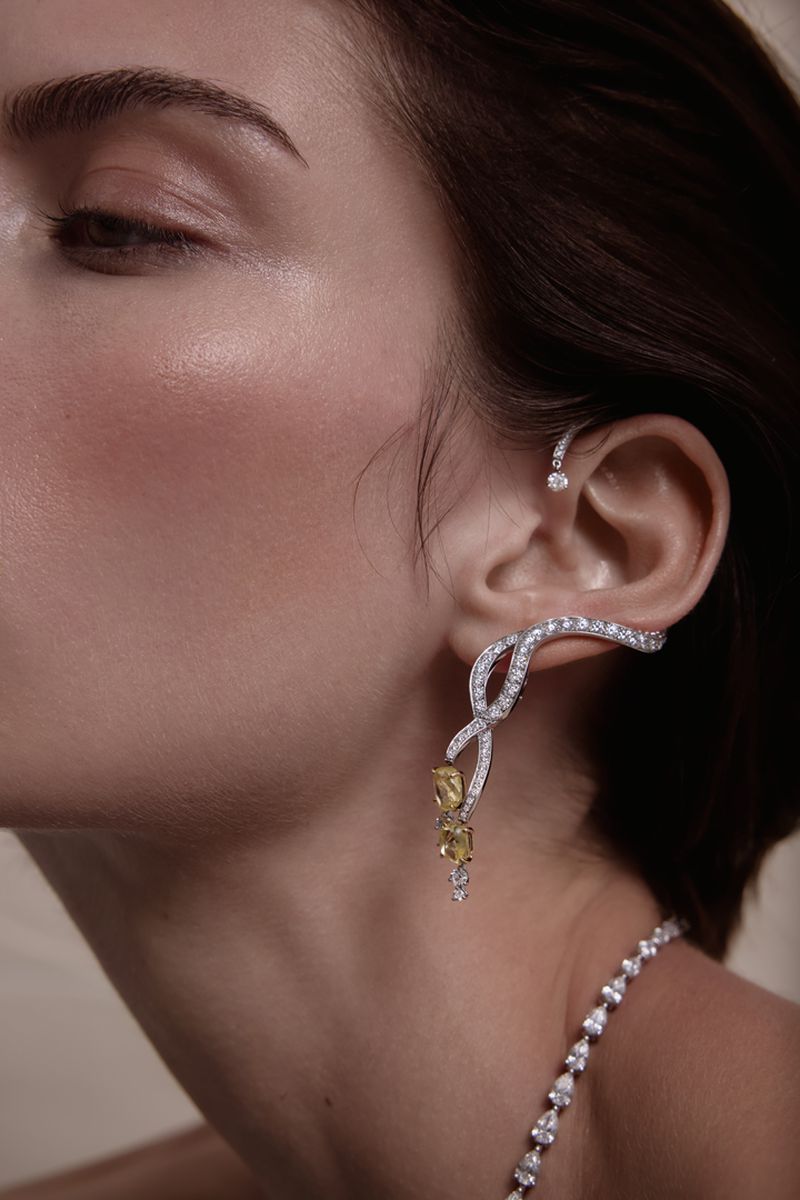 Close up profile of a woman wearing ornate diamond and yellow gemstone ear cuffs and a matching diamond necklace.