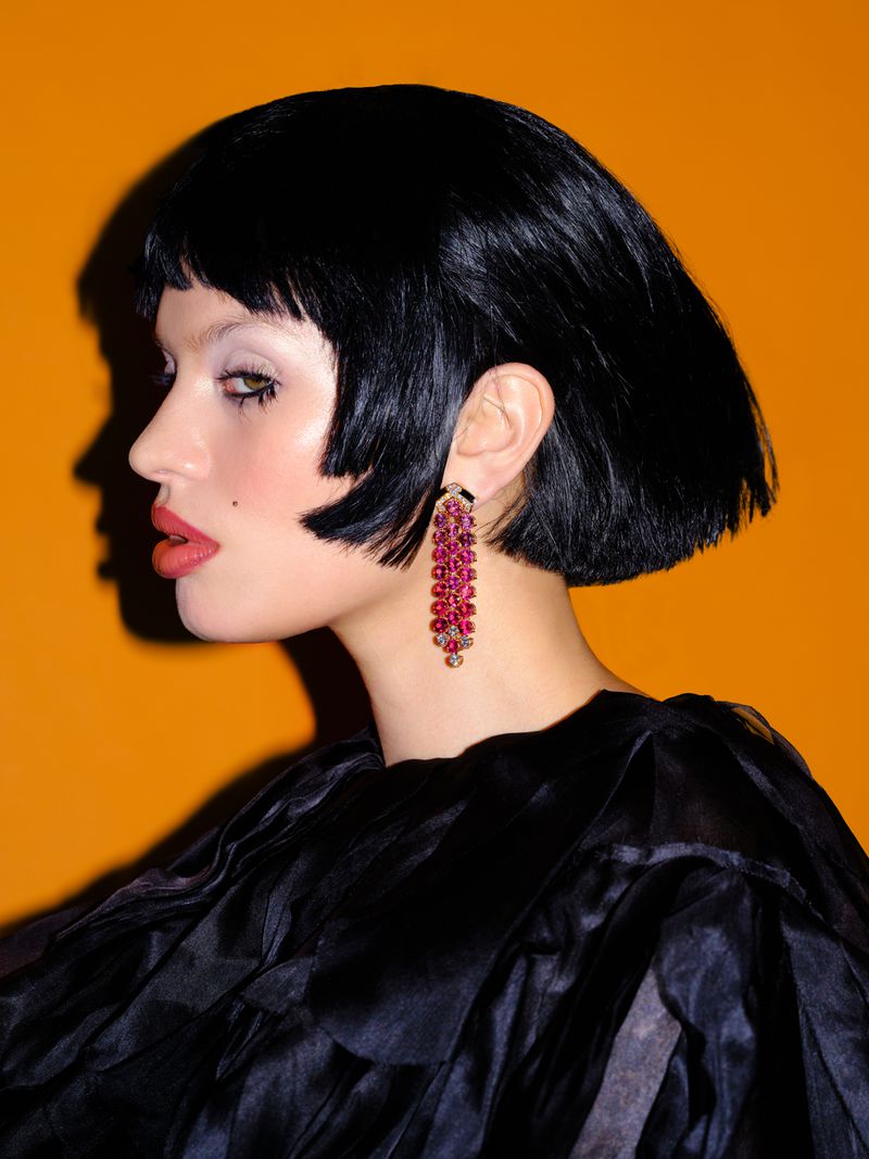Profile portrait of a model with short dark hair wearing a drop earring and dark top against an orange background