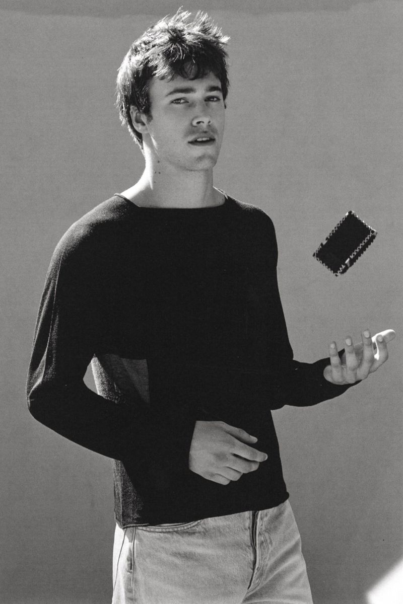Monochrome portrait of a young man wearing a black long-sleeve top against a plain studio background.