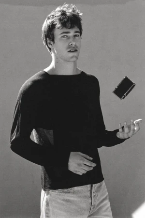 Monochrome portrait of a young man wearing a black long-sleeve top against a plain studio background.