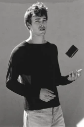 Monochrome portrait of a young man wearing a black long-sleeve top against a plain studio background.