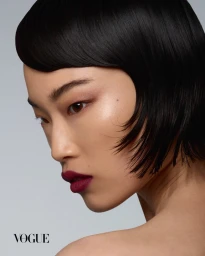 Close-up beauty portrait of a woman with short dark hair and deep berry lipstick against a neutral grey background
