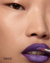 Close-up portrait of a model having purple lipstick applied with a brush for Vogue Thailand.