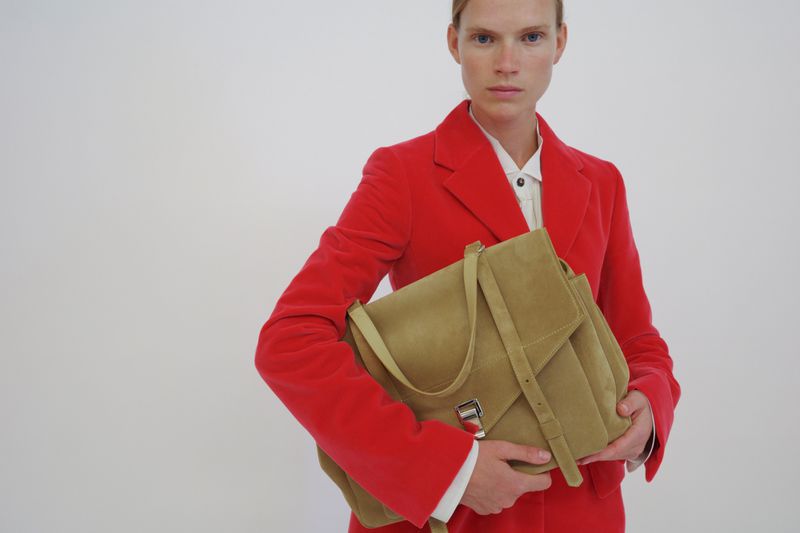 Model in a bright red blazer holding a tan shoulder bag against a plain white background for Proenza Schouler