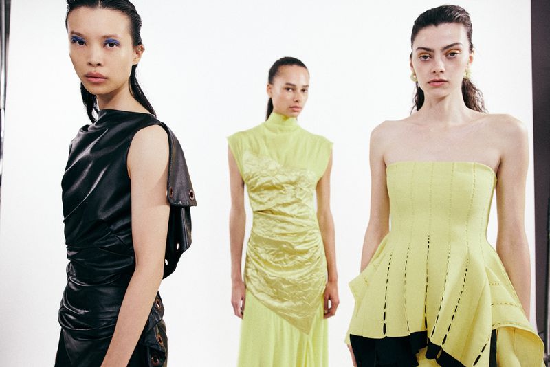 Three female fashion models in contemporary designer clothing posing against a bright white seamless studio background.