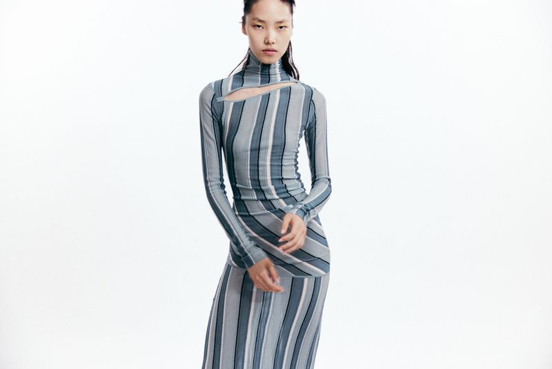 Model wearing a blue and grey striped turtleneck dress with a cutout detail against a white background