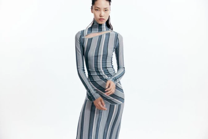 Model wearing a blue and grey striped turtleneck dress with a cutout detail against a white background