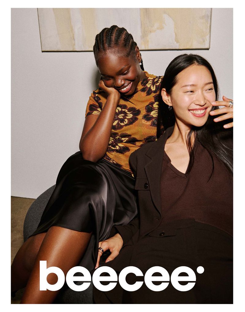 Two smiling female models posing together indoors for the Beecee 2026 campaign, wearing floral top and dark blazer.