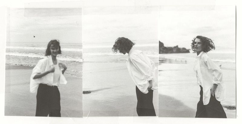 Black and white triptych of a female model wearing an unbuttoned white shirt and dark trousers walking along a sandy beach shoreline