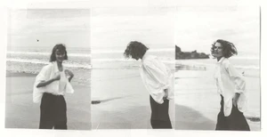 Black and white triptych of a female model wearing an unbuttoned white shirt and dark trousers walking along a sandy beach shoreline