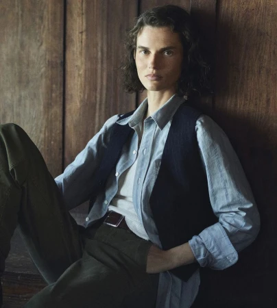 Model Giedre Dukauskaite wearing a blue shirt and dark vest against a wood background for Buck Mason.