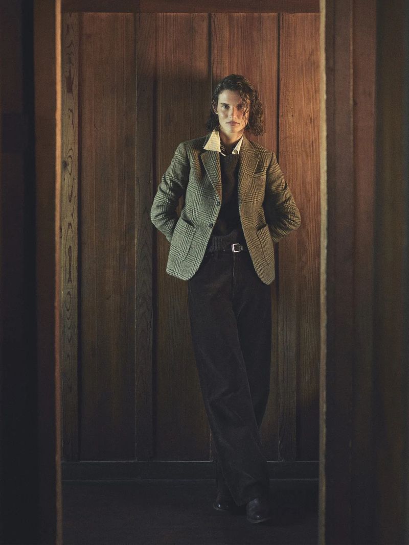 Model Giedre Dukauskaite wearing a tweed blazer and dark trousers standing against wood paneling for Buck Mason