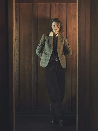Model Giedre Dukauskaite wearing a tweed blazer and dark trousers standing against wood paneling for Buck Mason