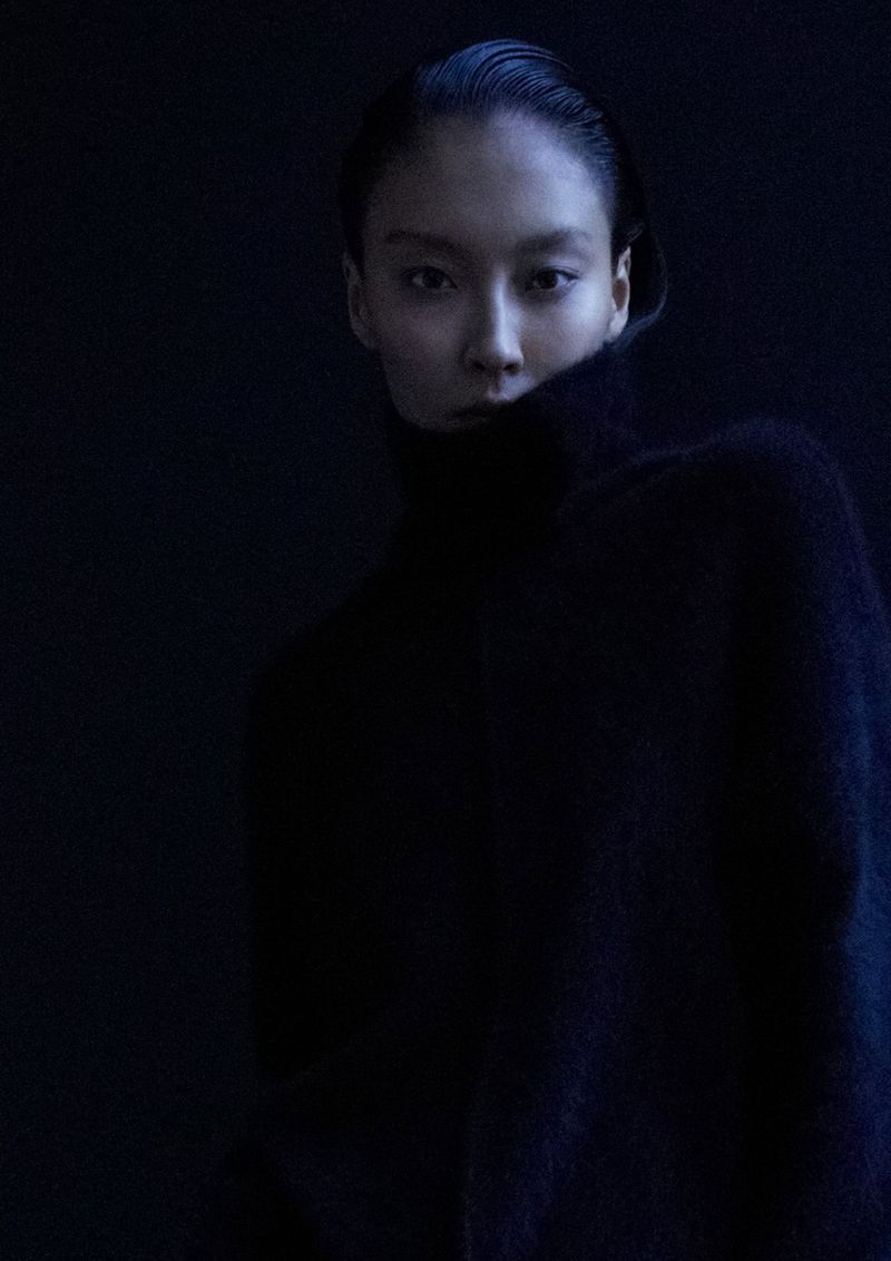 Model with slicked back dark hair wearing a black turtleneck sweater in low key lighting