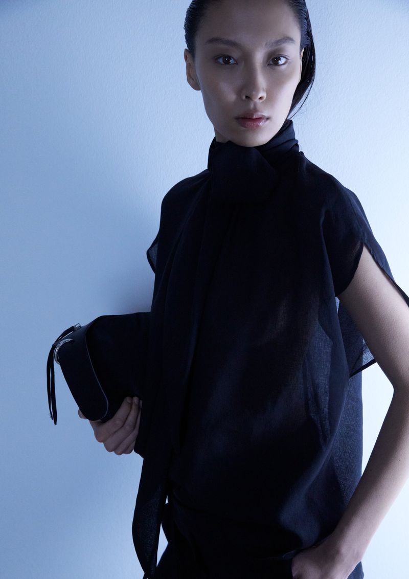 Model in black top holding a handbag against a plain background for Uli Schneider FW 2026 campaign photographed by Tamara Arne
