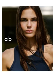 Portrait of a female model wearing a dark blue tank top with the Alo logo outdoors in natural light.