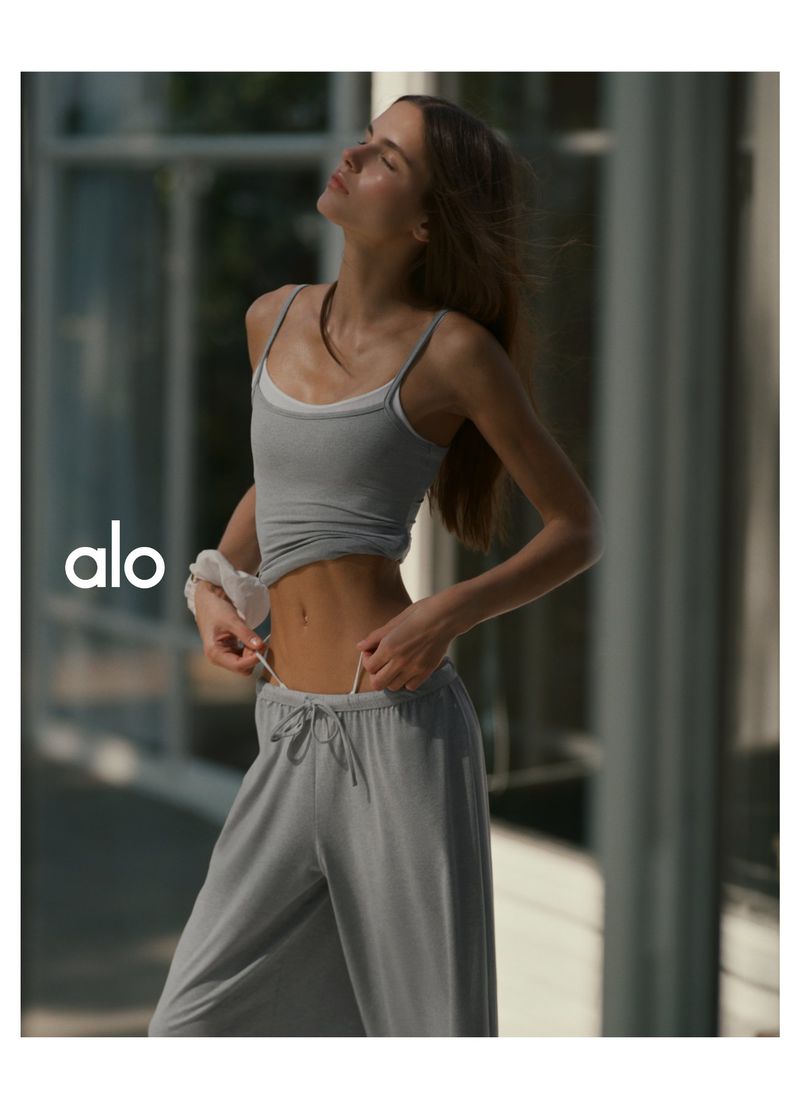 Model wearing grey tank top and sweatpants adjusting her waistband in daylight for Alo Faces of Fall project