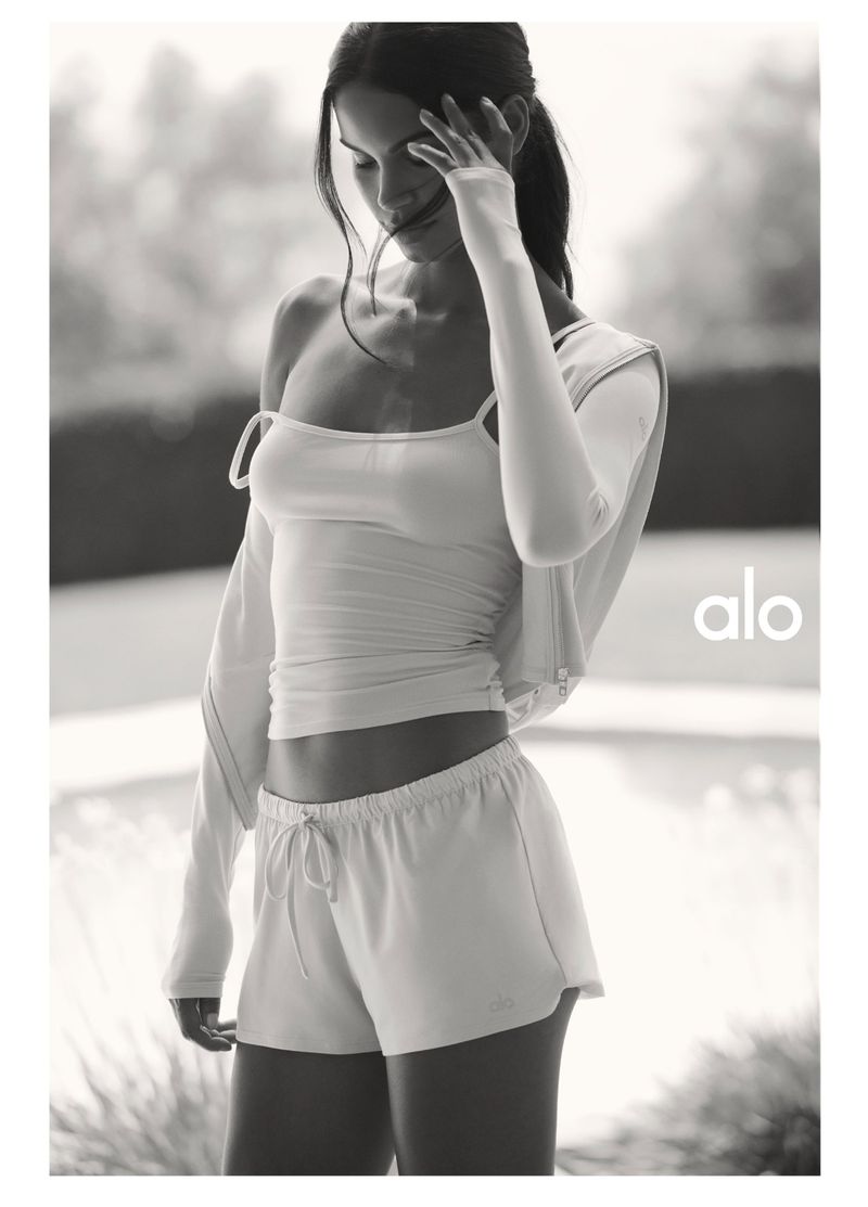 Monochrome fashion campaign image featuring a model wearing activewear shorts and a top for Alo.