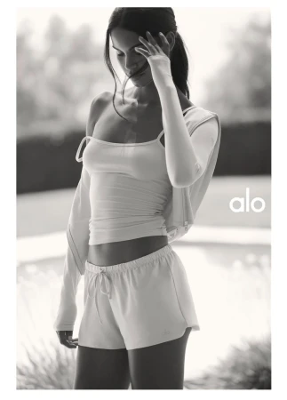 Monochrome fashion campaign image featuring a model wearing activewear shorts and a top for Alo.
