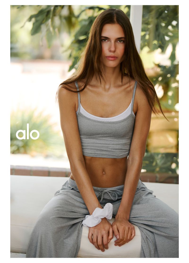 Model in grey crop top and matching sweatpants sitting outdoors against a natural garden backdrop for Alo.