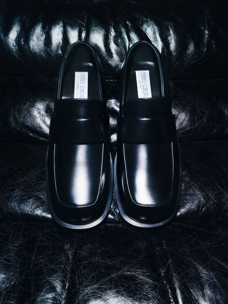 Pair of black leather loafers placed upright against a dark creased leather background.