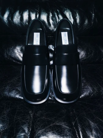 Pair of black leather loafers placed upright against a dark creased leather background.