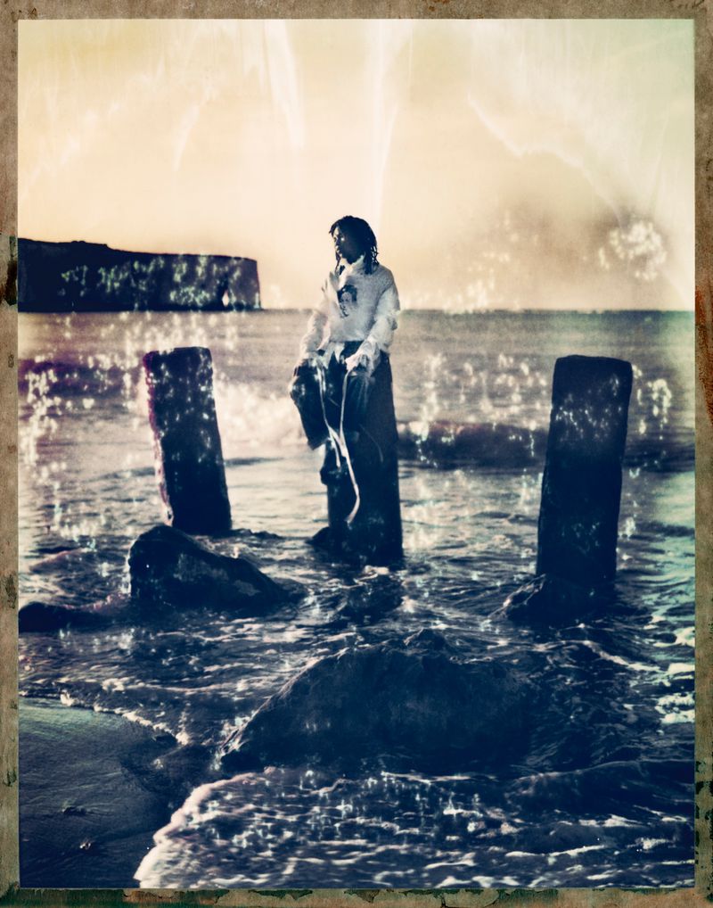 Model standing on a wooden post in the sea during a coastal sunset for Ann Demeulemeester campaign