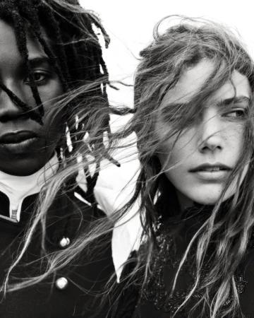 Close-up black and white portrait of two models with tousled hair against a plain bright background