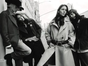 Black and white editorial fashion campaign image showing four models posed together on an urban street.