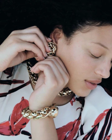 Close-up of a model putting on chunky gold jewelry while wearing a floral patterned top