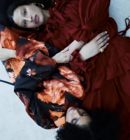 Two women lying down wearing red dresses and floral jackets against a neutral background