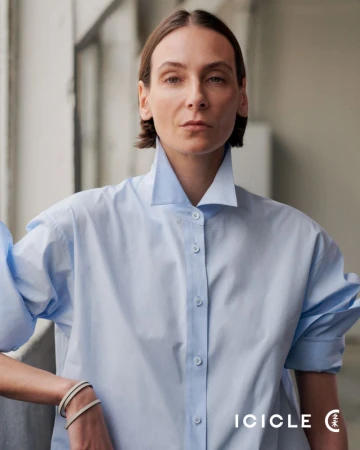 Model in a light blue button-down shirt with a stiff collar standing in an interior space for ICICLE.