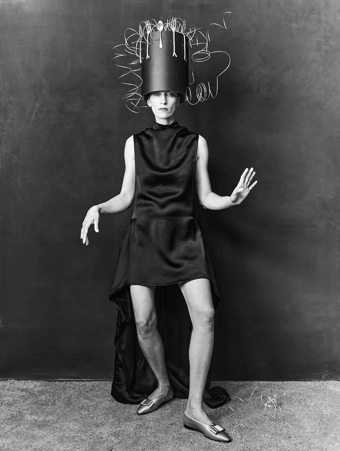 Model in black dress wearing sculptural wire-art hat standing against dark textured backdrop for 10 Magazine Deutsch