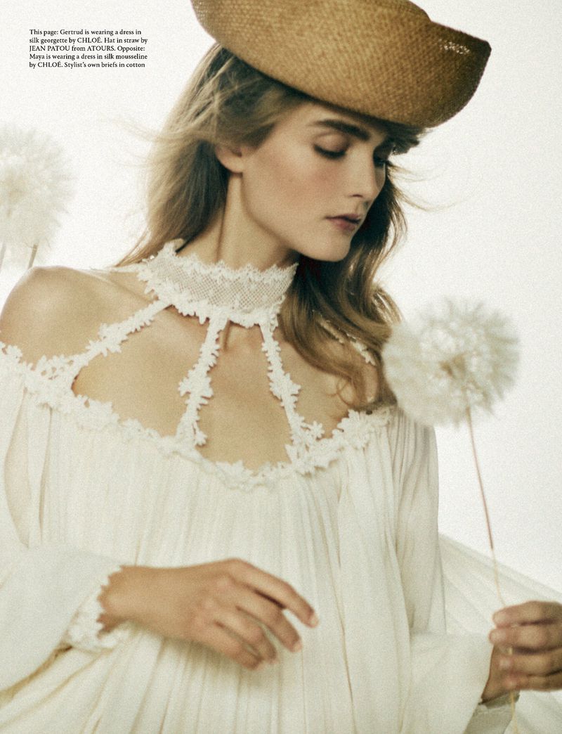 Model wearing a white lace-trim dress and straw hat holding a dandelion puff in an AnOther Magazine fashion editorial.