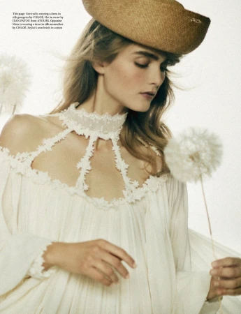 Model wearing a white lace-trim dress and straw hat holding a dandelion puff in an AnOther Magazine fashion editorial.