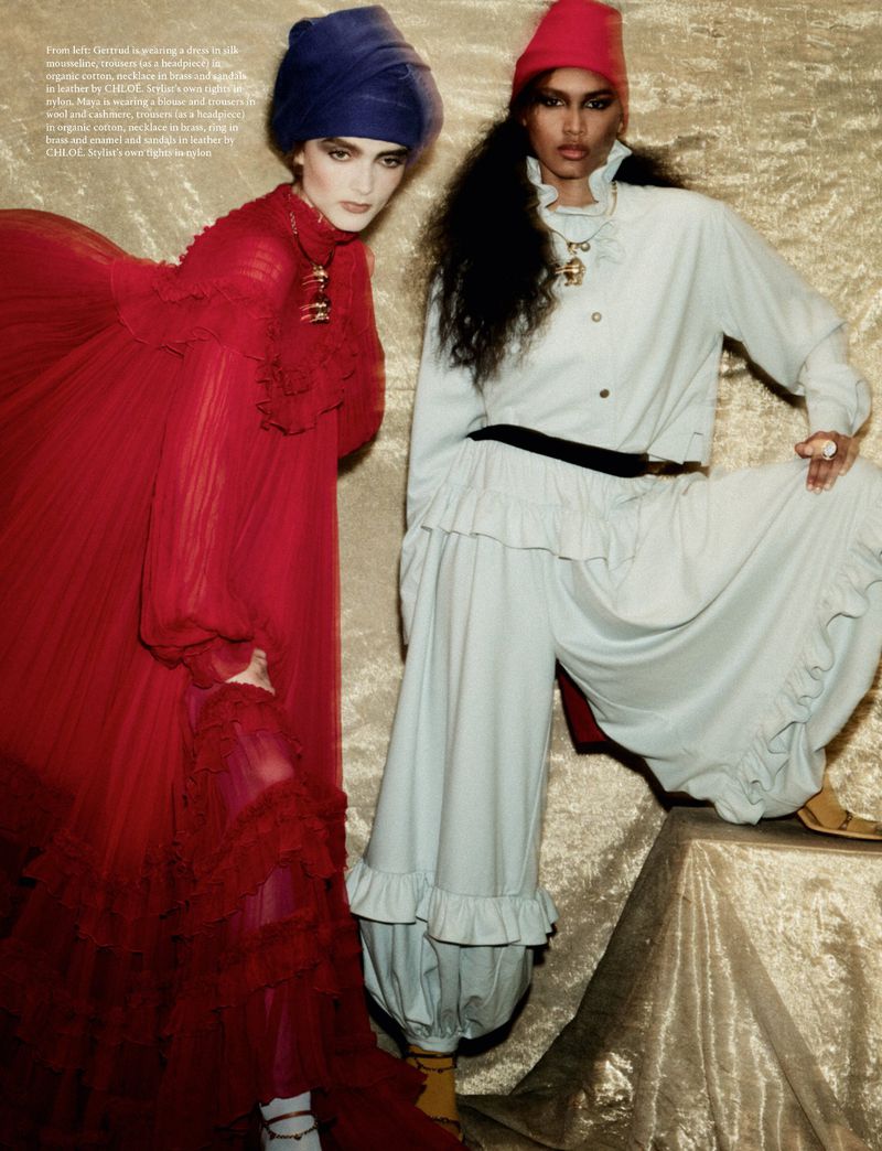 Two female models posing in layered red and pale blue outfits against a textured golden background