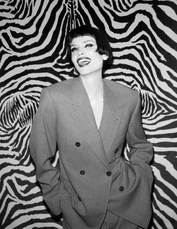 Model Natasha Poly wearing a structured grey double-breasted suit against a bold black-and-white zebra print background for Pop Magazine.