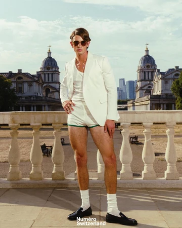 Man in a white blazer, white shorts, and sunglasses standing outdoors against a classic architectural backdrop.