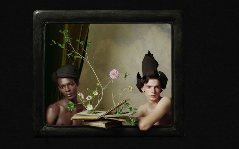 Two male models posing inside a framed tableau with a floral arrangement emerging from an open book, photographed by Kin Chan Coedel for AnOther Man China.